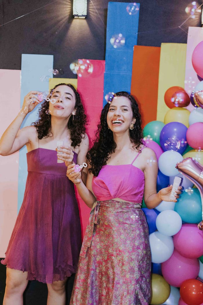 Two women enjoying bubbles at a cheerful party with vibrant decorations.